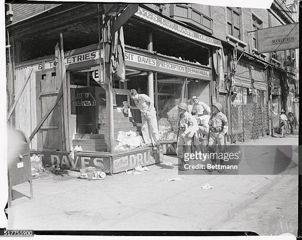 Two gun bearing M.P.'s offer protection to a workman cleaning up the window of a store wrecked during the rioting of whites and blacks in Detroit....