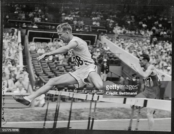 Hurdles star R. F. Ault is shown taking the 400-meter hurdles event in his stride to emerge victor over France's Yves Cros at the Olympic hurdles...