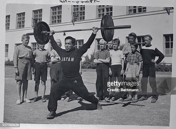 Finnish small fry stand around and watch Isamu Shiraishi, Japanese Bantam Weight Lifter, working out in preparation for the Olympic Games which open...