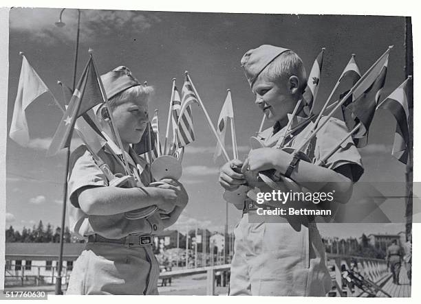 The young Finnish scouts, helpers at the Olympic Village at Helsinki, are carrying armfuls of national flags as Finland's capital prepares to greet...