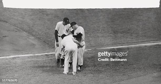 Coach Bill Dickey, and trainer Gus Mauch examine the knee of Yankee center fielder Mickey Mantle, who injured it beating out a bunt in the second...