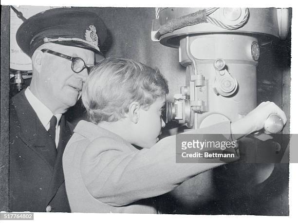 Little crown prince Carl Gustaf looks through a periscope at an exposition in Stockholm commemorating the 50th anniversary of the Swedish submarine...
