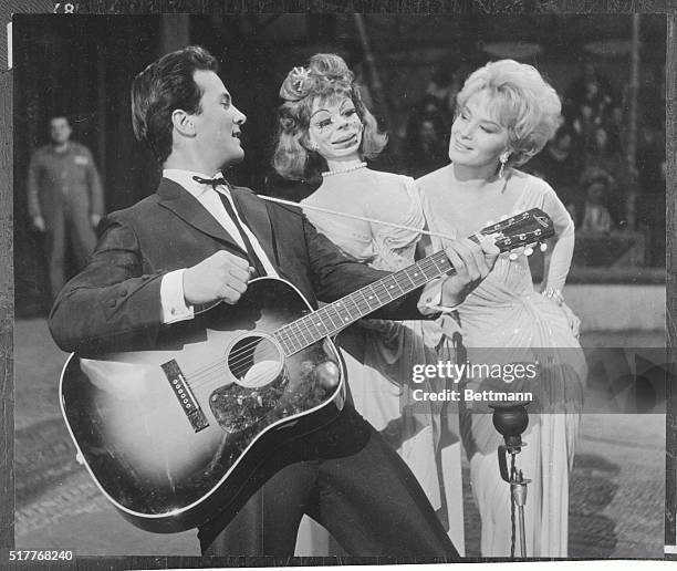 Strumming his trusty guitar, singer-actor pat Boone serenades a buxom dummy named Godiva in a scene for the seven parts Production of The Main...