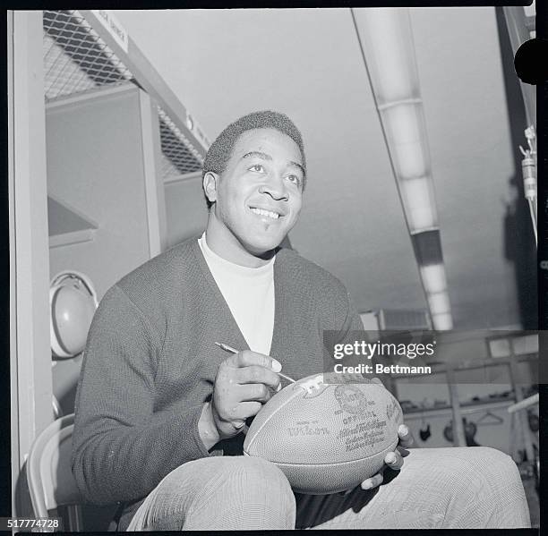 Leroy Kelly, Cleveland Browns halfback, close up in dressing room autographing football.