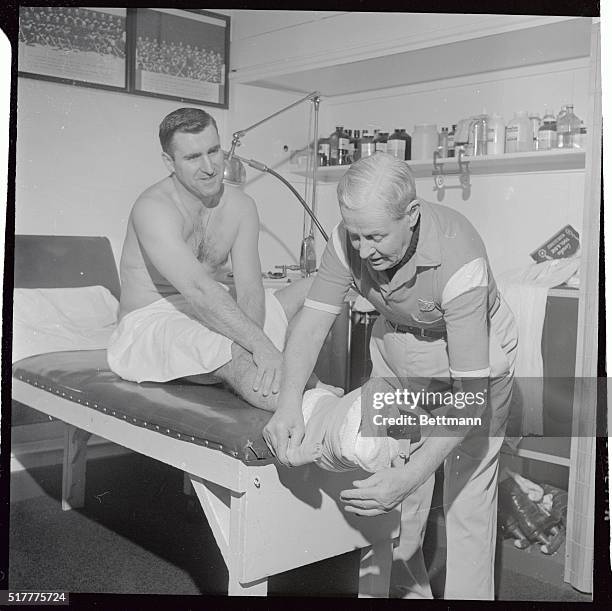 Photo shows Red Wing right winger Floyd Smith having an ice pack taped to his right foot here by clubhouse man Harry Watmuff, after he broke a small...