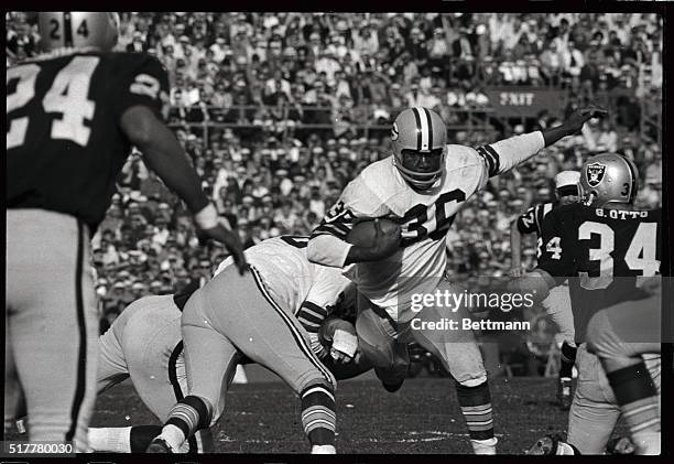 Photo shows a determined look on the face of Green Bay running back Ben Wilson as he charges toward Oakland linebacker Gus Otto, as he carries a hand...