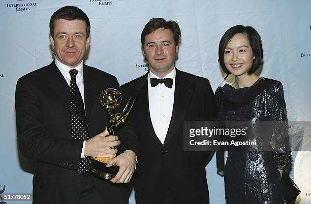 Peter Morgan and Francis Hopkinson pose with the 'TV Movie or Mini-Series' award with presenter Luyu Chen at the 32nd International Emmy Awards...