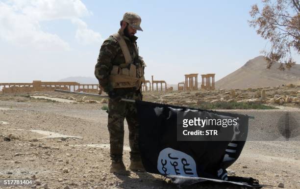 Member of the Syrian pro-government forces carries an Islamic State group flag as he stands on a street in the ancient city of Palmyra on March 27...