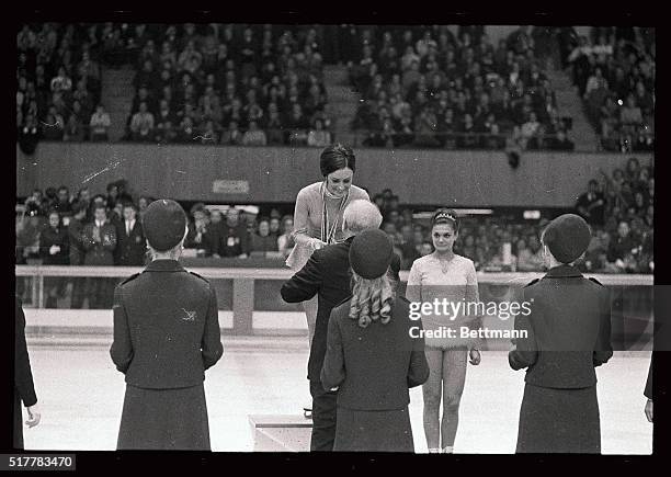 Peggy Fleming, the 19-year-old Olympic figure skating gold medalist from Colorado Springs, Colorado, is flanked on pedestal during medal presentation...