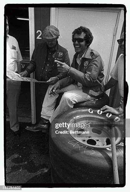 Perched on a stack of tires, three-time Purolator 500 winner Richard Petty jokes with colleagues prior to the start of time trials for the Coca Cola...