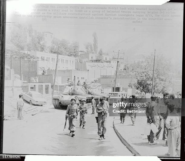 An American-made M-60A1 tank with mounted machine guns and soldiers posted on top guards a vital road in Paveh as a group of helmeted troops carrying...