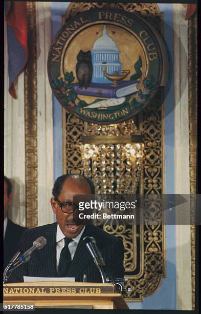 Addressing the National Press Club while standing beneath their insignia is Egyptian President Anwar Sadat.