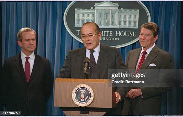 Director of the National Security Agency John M. Poindexter holds a press conference; he is flanked by President Reagan and an unidentified...