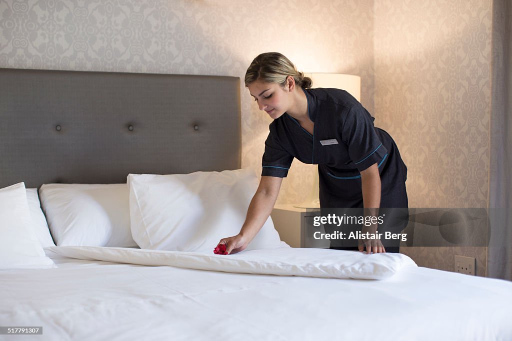 Chambermaid making bed in hotel room