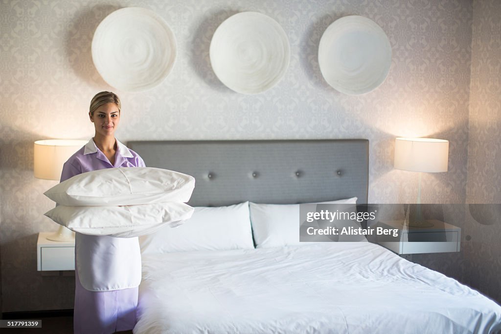 Chambermaid making bed in hotel room