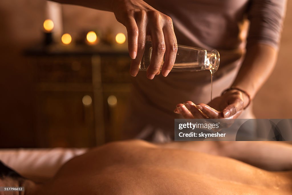 Close-up of massage therapist pouring massage oil in hand.