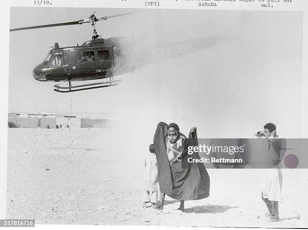 El Aaiun, Spanish Sahara: Old man has his robes blown up in a cloud of dust as helicopter takes off from this desert capital, while youth covers both...