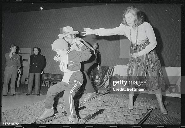 New York: Mrs. Eunice Kennedy Shriver helps a youngster down a special ski ramp with Olympic medalist Billy Kidd as coach during a press announcement...