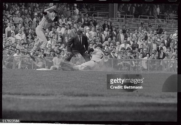 Baltimore's Brooks Robinson leaps high to get a throw from outfielder Jackie Brandt, as Yankees' Mickey Mantle slides into third base under the...