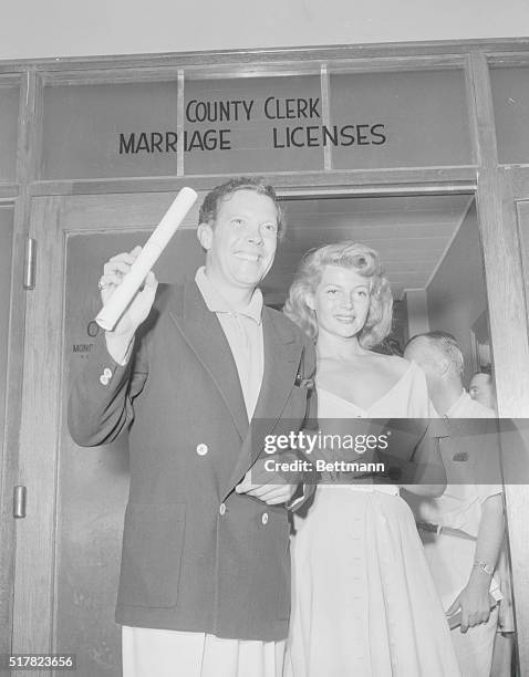 To the tune of popping flashbulbs, Rita Hayworth and Aly Khan stroll arm in arm towards the waiting newsmen to begin their giant sized press...