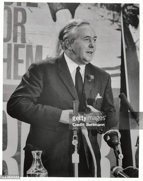 Although wearing a dark suit and boutonniere, Harold Wilson presents a casual picture as he faces microphones with a pipe in his hand. The British...