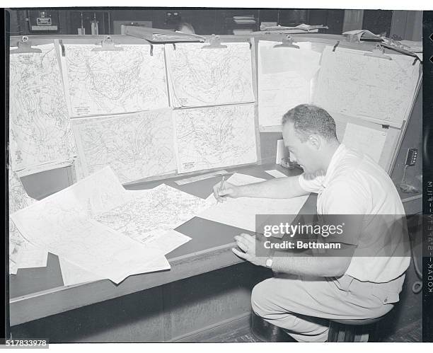 Milton J. Fayne, meteorologist at the New York Weather Bureau, scans a large number of weather charts to get a line on the activities of Hurricane...