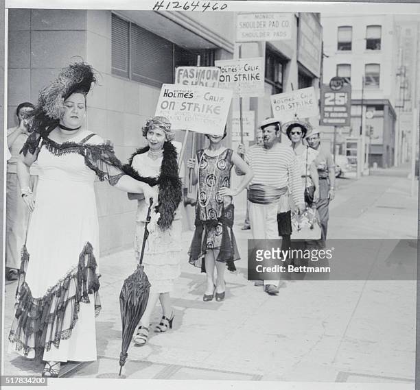 Wearing costumes that were the Vogue in by gone decades, members of the International Ladies Garment Workers' Union are shown picketing the Holmes of...