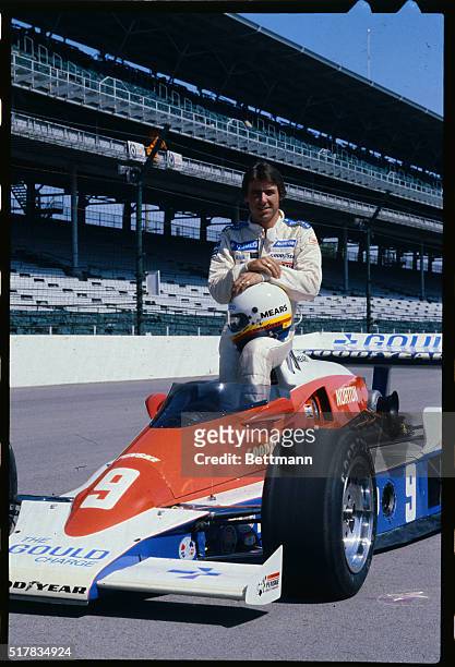 Rick Mears is shown sitting on his Indy car, wearing his racing outfit and holding his helmet in his lap.
