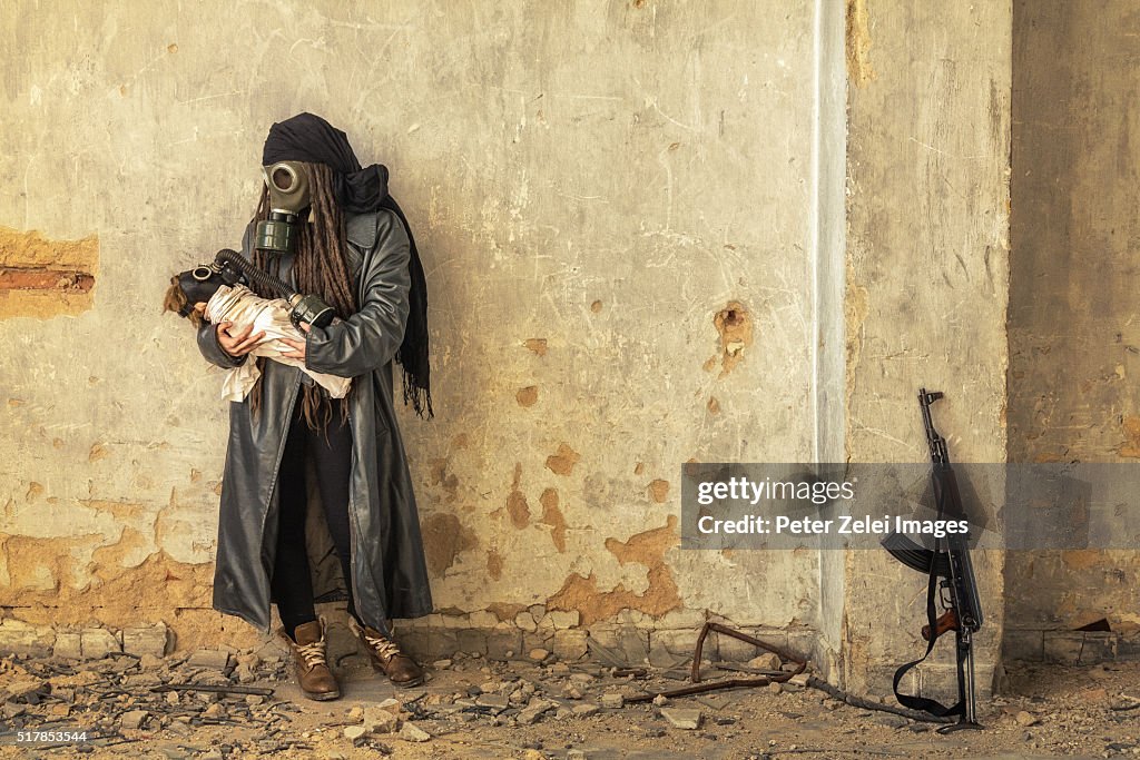 Post apocalyptic survivor holding her baby in gas mask