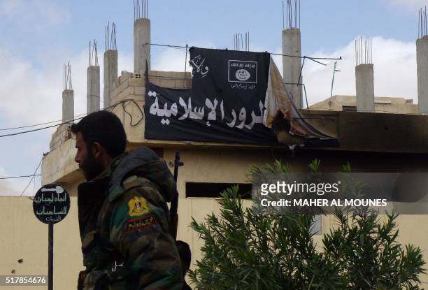 Member of the Syrian government troops walks past a banner bearing Islamic State group slogans in the damaged streets of the residential...
