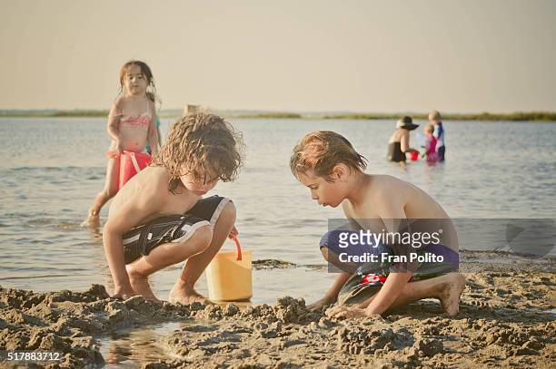 Children filling buckets and playing in sand at the beach.