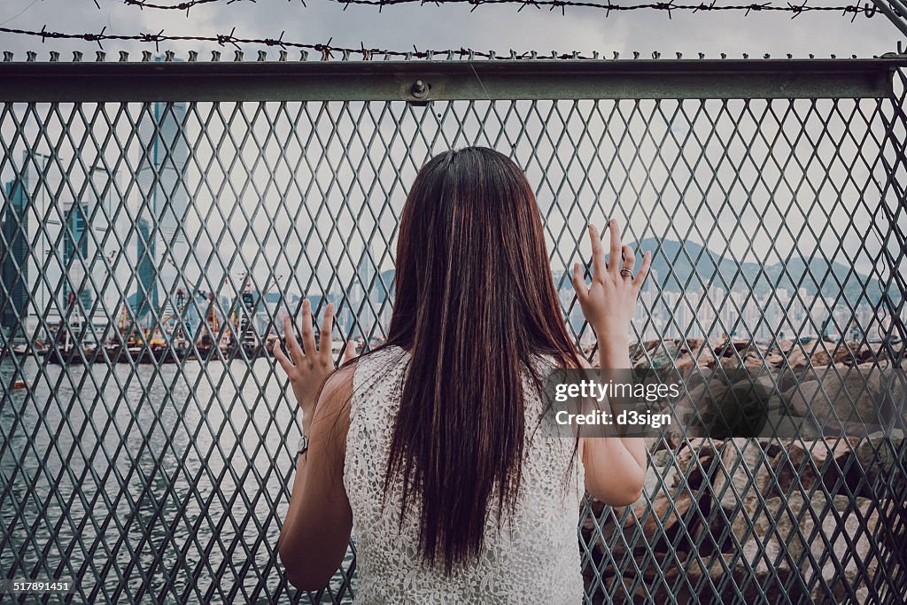 Female standing in front of fence looking at city