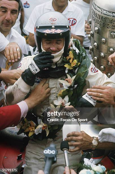 Race car driver Mario Andretti is greeted at his car with his trophy, his crew, and reporters after winning the Indianapolis 500 at the Indianapolis...