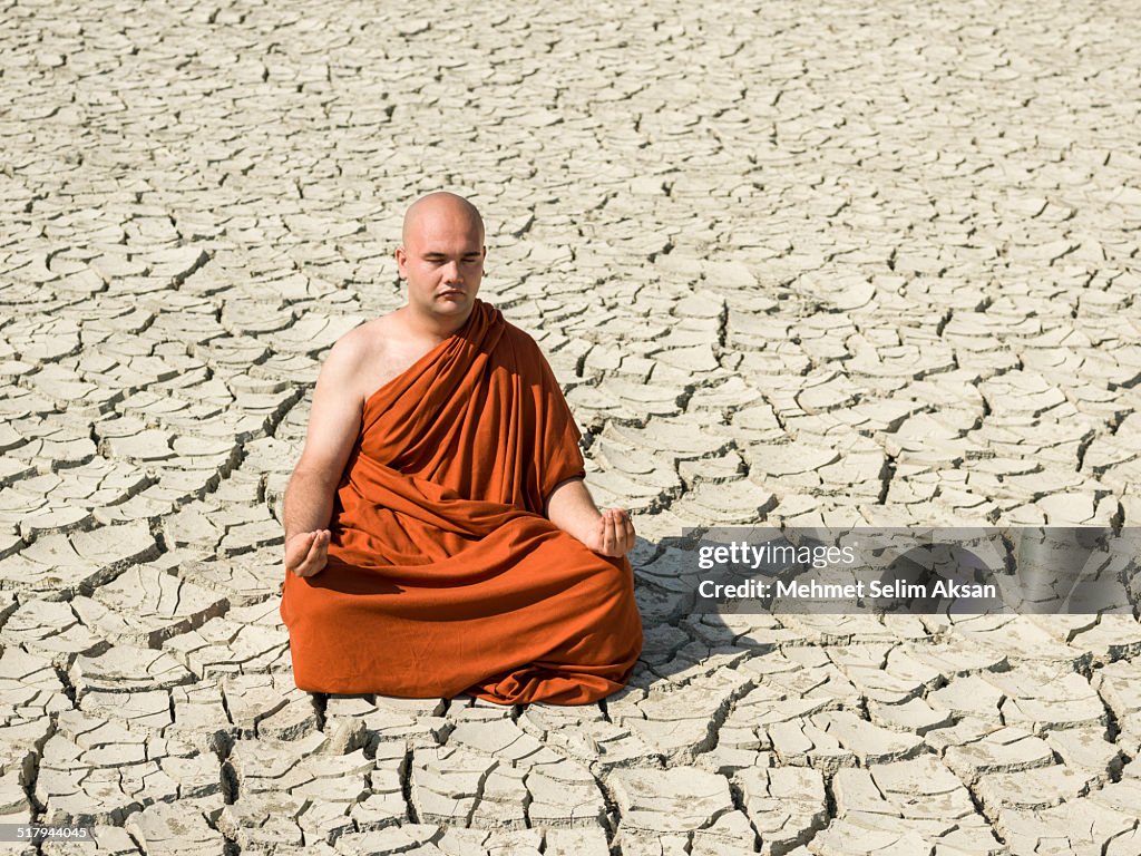 Buddhist monk meditating on cracked earth