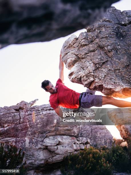 rock climber with hand in chalk bag hanging on boulder - overhangende rots stockfoto's en -beelden