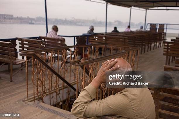 Commuter enjoys a peaceful few minutes on the top deck of the state-run ferry across the River Nile at Luxor, Nile Valley, Egypt. Resting his head on...