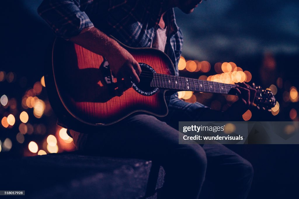 Hipster guitarist playing on a rooftop at night