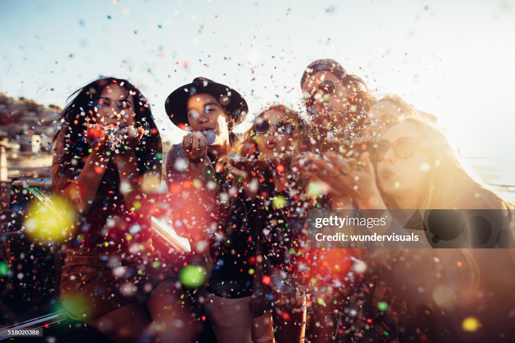 Adolescente hipster amigos celebrar por soplado colorido confeti de manos