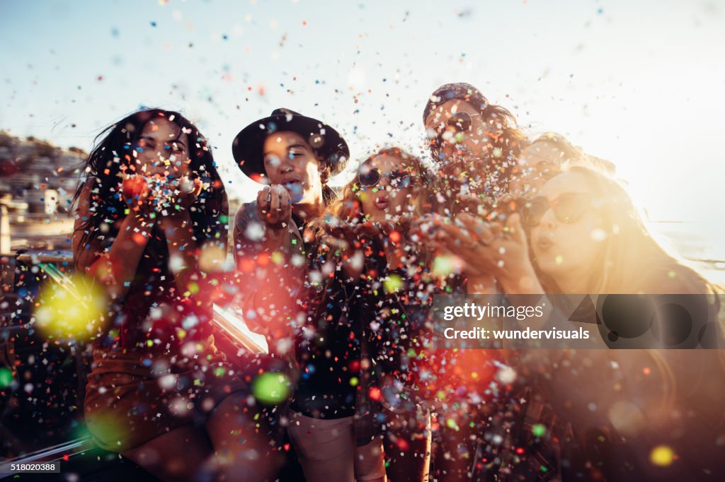 Teenager hipster friends celebrating by blowing colorful confetti from hands