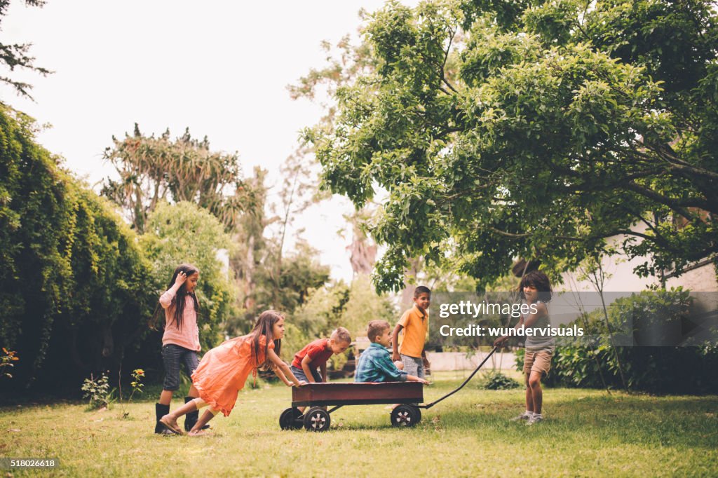 Children pushing and pulling friends in red wagon in park