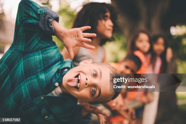 little boy pulling a funny face with friends in background - funny face stockfoto's en -beelden