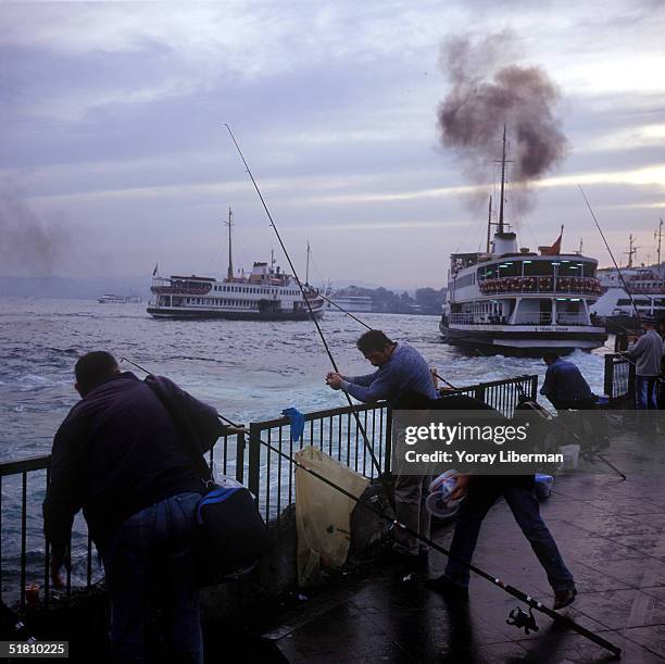 Turkish men fish on the Eminonu ferry station pier on the European side of Istanbul's Bosphorus Strait early in the morning on October 19, 2004 in...