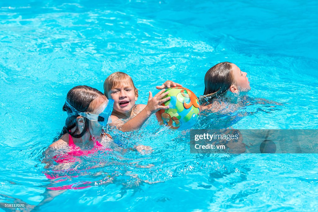 Trois enfants jouant avec un ballon dans la piscine