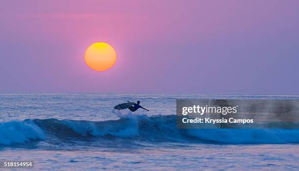 surfer jumping with his board at sunset on the beach playa carmen in santa teresa - península de nicoya fotografías e imágenes de stock