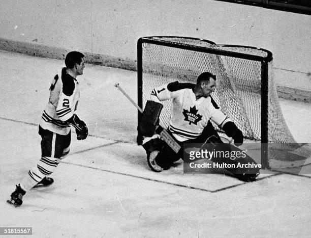 Canadian ice hockey player Johnny Bower of the Toronto Maple Leafs minds the net as fellow Leaf Larry Hillman skates back to help out during the...