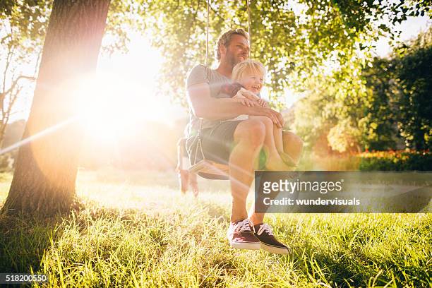 vater und seine lachen sohn genießen sie den sommer sonnenuntergang auf schaukel - schaukel stock-fotos und bilder