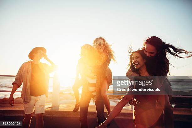 friends having piggyback rides on beach at sunset - strand party stockfoto's en -beelden