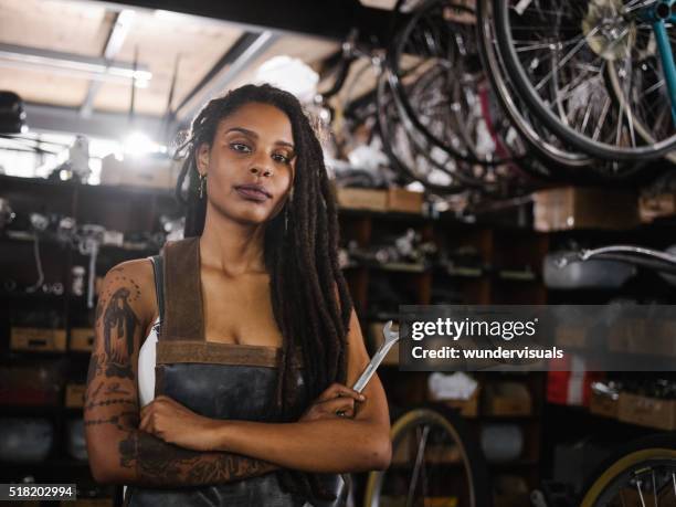 afro woman bicycle mechanic looking proud in bike repair worksho - tattoo woman stock pictures, royalty-free photos & images