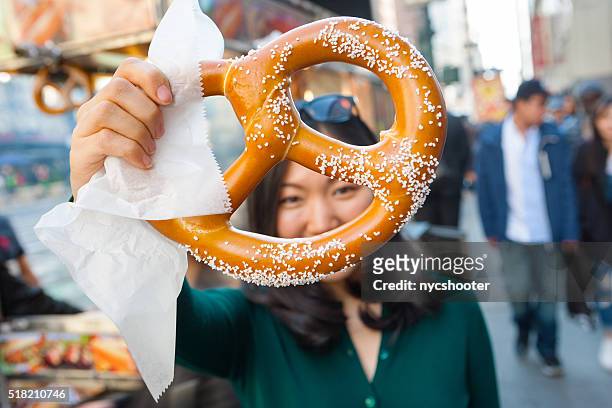 young asian girl holding pretzel in nyc - pretzel stock pictures, royalty-free photos & images