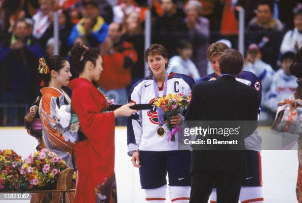 Members of the United States women's hockey team stand as an unidentified man in a suit and two women in kimonos award them medals and flowers after...